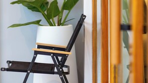 Un coin avec un pot de fleurs blanc contenant une plante en pot et une chaise pliante noire.