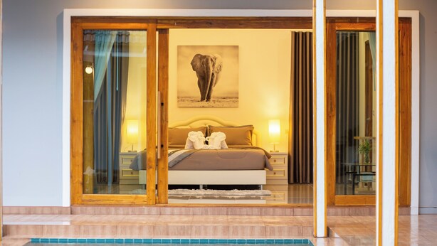 Une chambre avec un grand lit, une porte vitrée donnant sur un balcon et une piscine au premier plan.