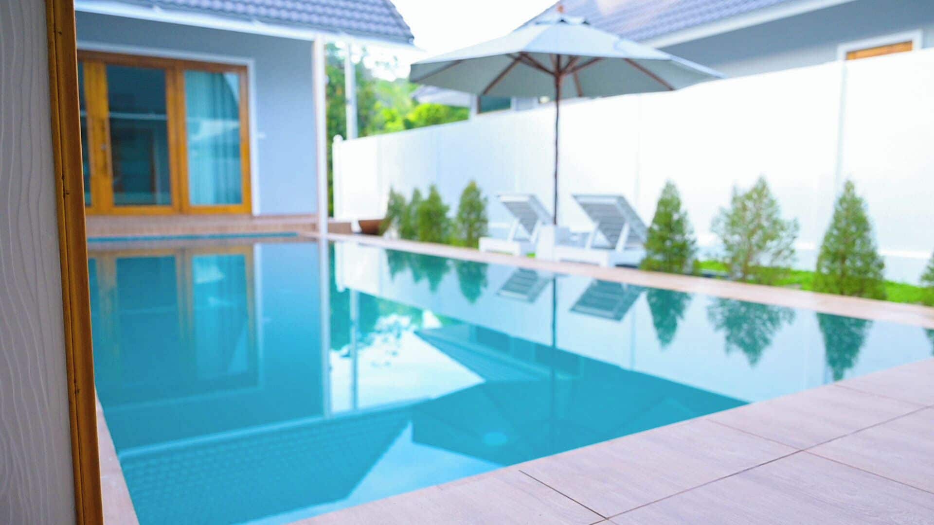 Una piscina con agua azul cristalina, rodeada por un muro blanco y un suelo de baldosas.