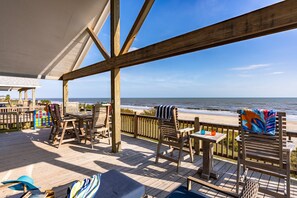 Eine Holzterrasse mit Sitzgelegenheit im Freien mit Blick auf Strand und Meer.
