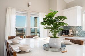 Une cuisine moderne avec une table à manger pour quatre personnes, une grande plante en pot et une vue sur la mer par les fenêtres.