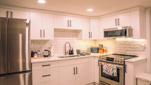 A modern kitchen with stainless steel appliances, white cabinetry, and a tiled backsplash.