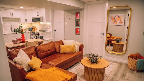 A modern living room with a brown leather sofa, a round wooden coffee table, and a kitchen in the background.