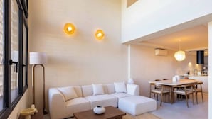 Uma sala de estar moderna com um sofá modular branco, uma mesa de centro de madeira e um espaço de jantar com mesa e cadeiras de madeira.