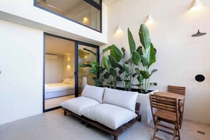 Quarto moderno com cama, sofá, mesa de jantar e plantas verdes grandes.