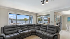 Ett modernt vardagsrum med en stor hörnsoffa, stora fönster med utsikt över en sjö och ett ljust, luftigt tak.