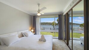 Ett hotellrum med en stor säng, en takfläkt, ett nattduksbord med en lampa och utsikt över en sjö och kullar.
