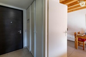 A room with a dark wooden door, a white wall, and a dining area with a wooden table and chairs. - LES CAMPANULES B - BOURG SAINT MAURICE (BOURG SAINT MAURICE)