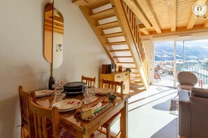 A dining area with a wooden table set for two, a wooden staircase, and a view of a town through large windows. - LES CAMPANULES B - BOURG SAINT MAURICE (BOURG SAINT MAURICE)