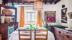 Un comedor con una mesa lista para cuatro, sillas de madera, una lámpara colgante y una pared de piedra con elementos decorativos.