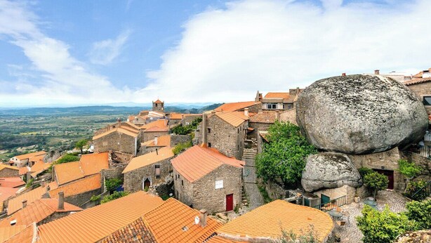 Un pueblo histórico con edificios de piedra y una gran formación rocosa.
