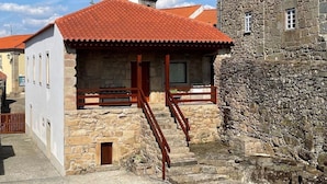 Un edificio de piedra con techo de tejas rojas, una escalera de madera y una pequeña ventana.