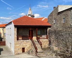 Un edificio de piedra con techo de tejas rojas, una escalera de madera y una pequeña ventana.
