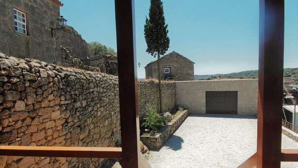 Un muro de piedra, un pequeño edificio con una puerta y un cielo despejado.
