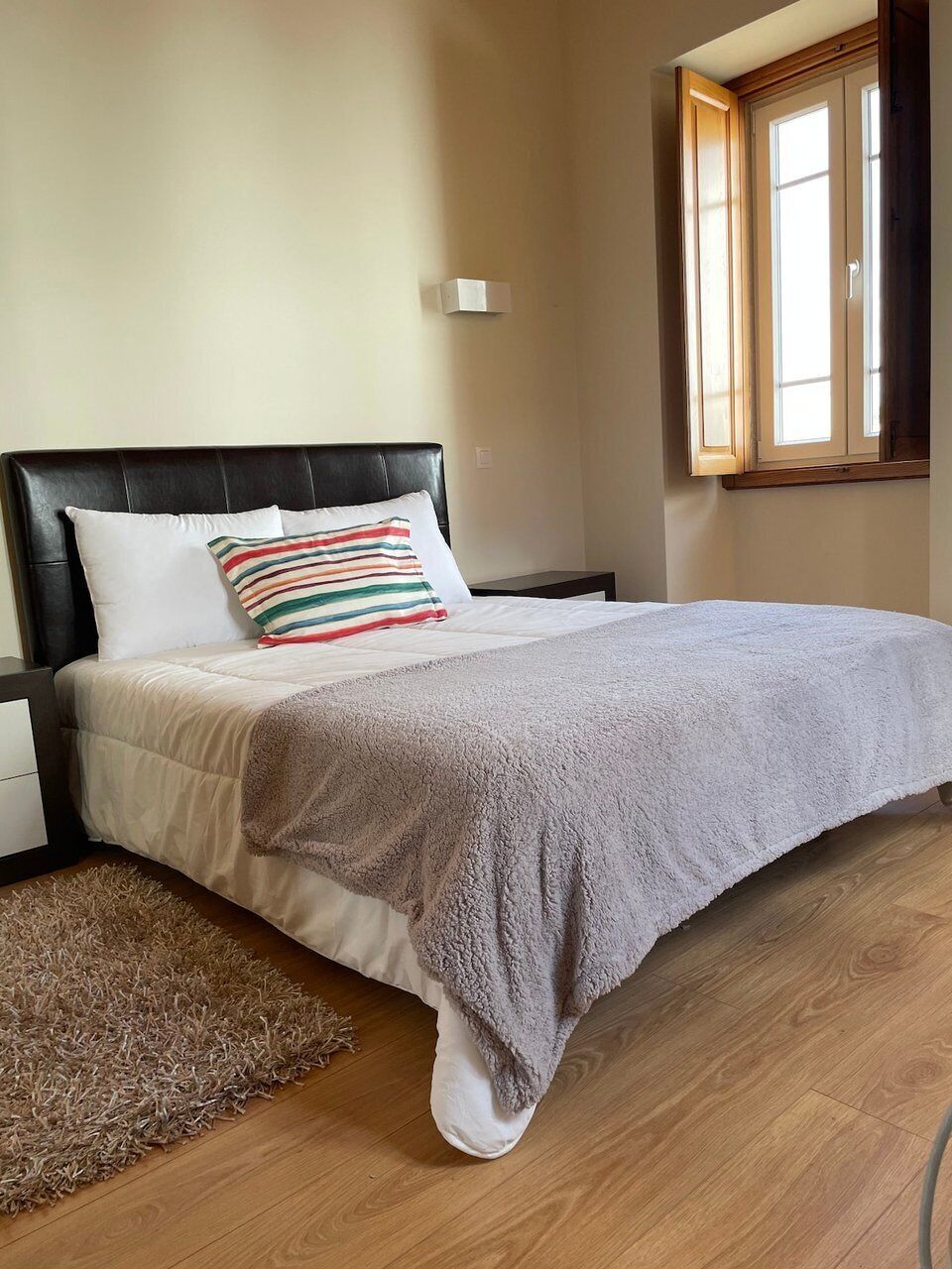 Une chambre à coucher avec un lit, une table de chevet, une fenêtre et un plancher en bois.