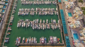 A marina with numerous boats docked in rows, adjacent to a hotel with multiple swimming pools and sun loungers. - Clube Albufeira - 2BR Pool, Kids Club & Family Fun (Albufeira)