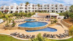 A resort with a large pool, sun loungers, and a building with multiple balconies. - Clube Albufeira - 2BR Pool, Kids Club & Family Fun (Albufeira)
