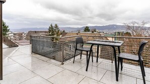 Eine Dachterrasse mit Tisch und Stühlen, einem Metallzaun und Blick auf Stadt und Berge.