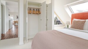 Ein Schlafzimmer mit einem großen Bett, einem Fenster mit Blick, einem begehbaren Kleiderschrank und einer Küchenzeile im angrenzenden Raum.