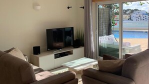 Un salon moderne avec un téléviseur à écran plat, une table basse en verre et deux canapés.