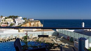 Un espace piscine aménagé sur le toit, avec des chaises longues et une vue sur la mer et les bâtiments.