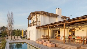 Un área junto a la piscina con terraza de madera, sillas de descanso y zona de comedor con asientos exteriores.