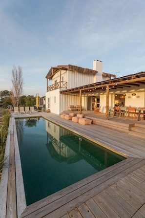 Ein Poolbereich mit Holzterrasse, Liegestühlen und Essbereich mit Gartenmöbeln.