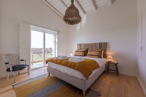 Ein Schlafzimmer mit Bett, Stuhl, Nachttisch, Lampe und Blick durch eine Glastür.