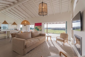 Ein geräumiger Wohnbereich mit Sofa, Sesseln, einem Esstisch und einem großen Fenster mit Blick ins Freie.