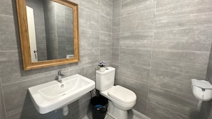 A bathroom with a wooden-framed mirror, a white sink, a toilet, and a trash bin. - Kuching Holiday Family Home @ Riverine Kuching (Kuching)