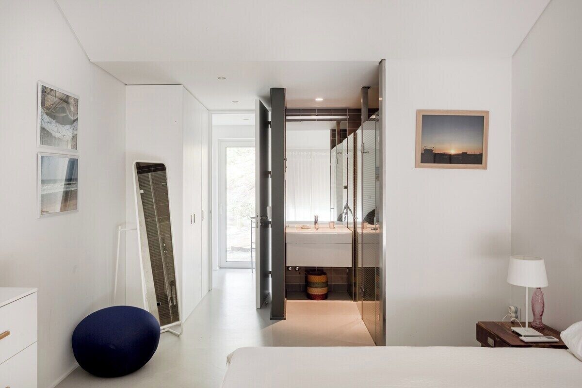 Una habitación de hotel moderna con una cama, una mesita de noche, una lámpara, un espejo y vistas al baño.