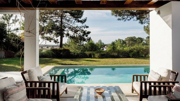 Zona junto a la piscina con mobiliario de madera y vistas a la piscina y la vegetación circundante.