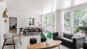 Ett rymligt vardagsrum med ett matbord, en soffa och ett soffbord. Stora fönster ger utsikt över omgivningen.
