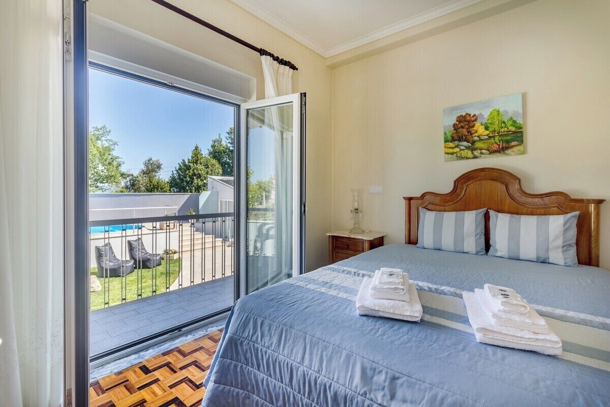 Une chambre à coucher avec un lit, un tableau accroché au mur et un balcon aménagé avec du mobilier d’extérieur.