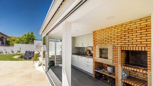 Een moderne keuken met een bakstenen openhaard, witte kasten en een glazen deur naar een terras.