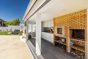 Eine moderne Küche mit Kamin aus Ziegelsteinen, weißen Schränken und einer Glastür, die auf eine Terrasse führt.