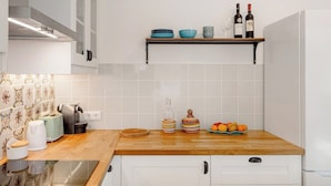 Eine Küche mit weißen Schränken, einer Holzausziehtafel, einer Kaffeemaschine, einem Toaster, einem Wasserkocher, einer Weinflasche und einer Schüssel mit Obst.