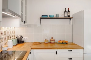 Eine Küche mit weißen Schränken, einer Holzausziehtafel, einer Kaffeemaschine, einem Toaster, einem Wasserkocher, einer Weinflasche und einer Schüssel mit Obst.