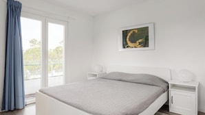 Ein Schlafzimmer mit einem Bett, einem Fenster mit Vorhängen, einem Nachttisch, einer Wandlampe und einem Gemälde.