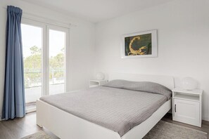 Ein Schlafzimmer mit einem Bett, einem Fenster mit Vorhängen, einem Nachttisch, einer Wandlampe und einem Gemälde.