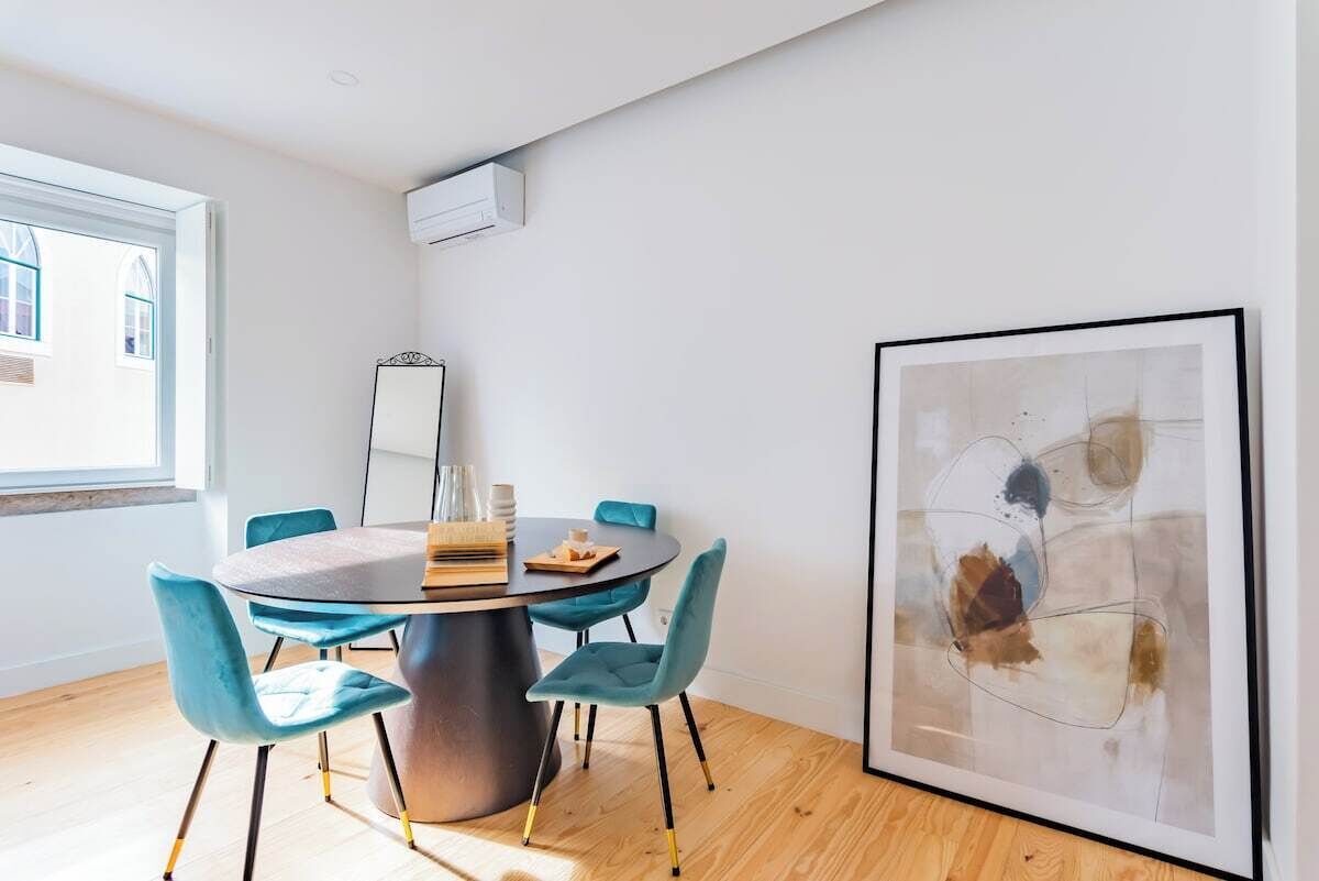 Un comedor moderno con una mesa redonda, sillas azules, un cuadro abstracto enmarcado y una ventana con luz natural.
