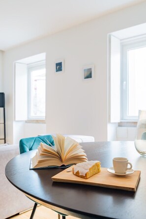 Ein runder Tisch mit einem offenen Buch, einer Kuchenscheibe und einer Kaffeetasse.