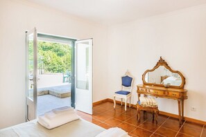 Una habitación con cama, tocador con espejo, silla y puerta que da a un espacio exterior.