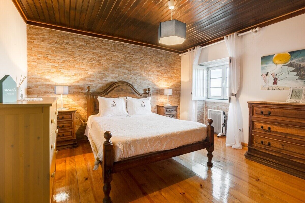 Une chambre avec un lit en bois, un mur en briques, une commode en bois, une table de chevet et un tableau accroché au mur.