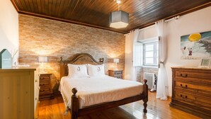 A bedroom with a wooden bed, a brick wall, a wooden dresser, a nightstand, and a painting on the wall.