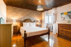 A bedroom with a wooden bed, a brick wall, a wooden dresser, and a window with curtains.