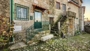 A stone building with a green door, a staircase, and a cobblestone courtyard.