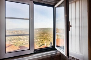 A window with a view of a hilly landscape and a distant town.