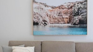 Ein beiges Sofa mit weißer Decke und grauem Kissen vor einer Wand mit einem gerahmten Landschaftsbild.