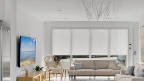 Ein modernes Wohnzimmer mit einer Couch, Sesseln, einem Holzesstisch und einem an der Wand befestigten Fernseher.